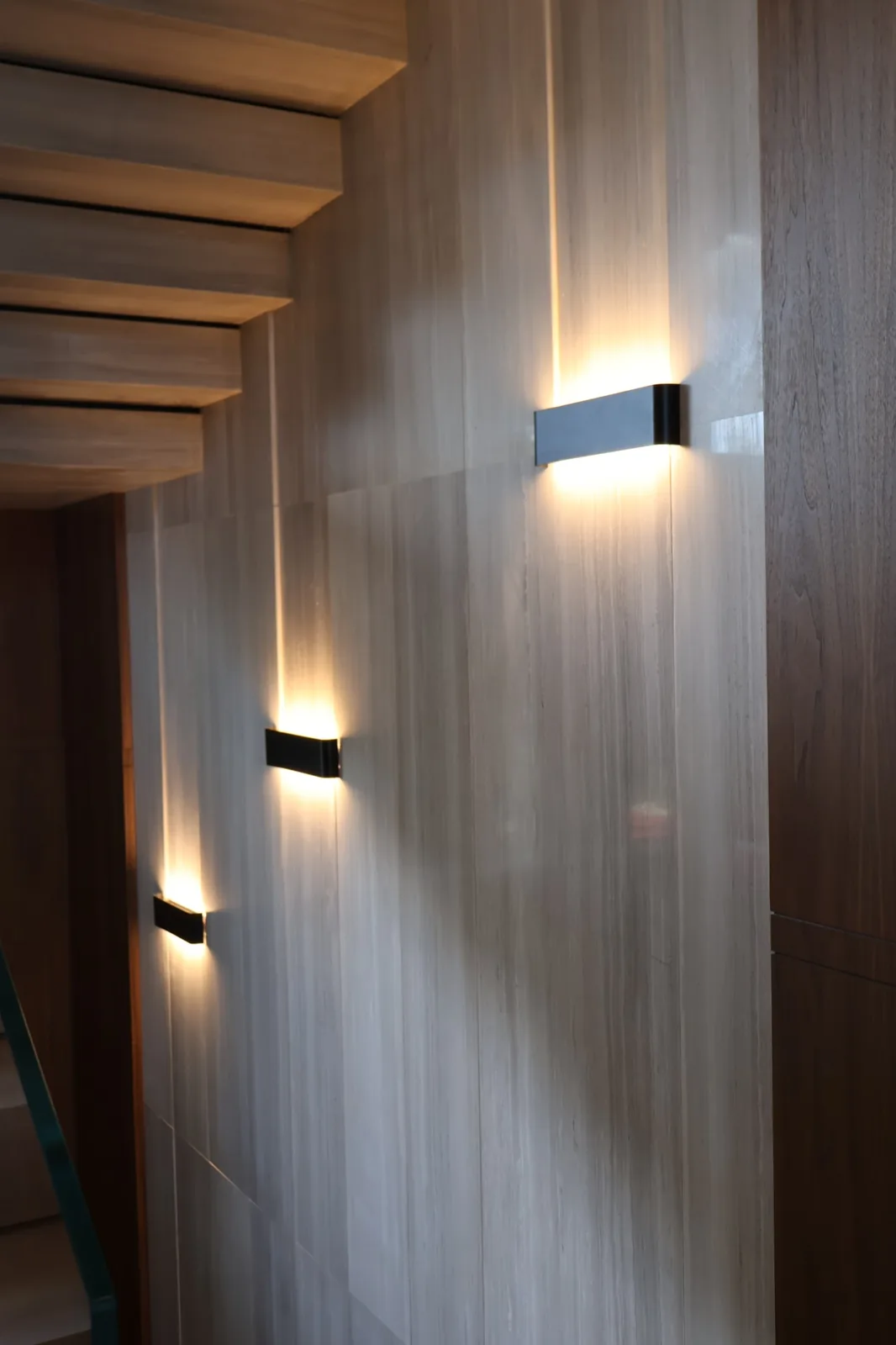 Arca Konakları — Up-and-down wall luminaires climb the travertine stairwell, grazing the stone with warm 3000K light.