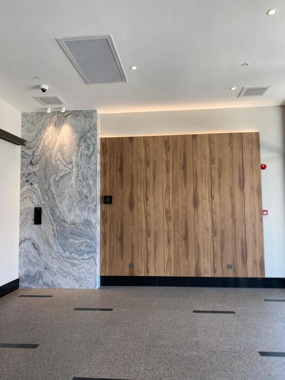 Tona Residence — The residential lobby: concealed cove light and recessed downlights across book-matched stone and walnut.