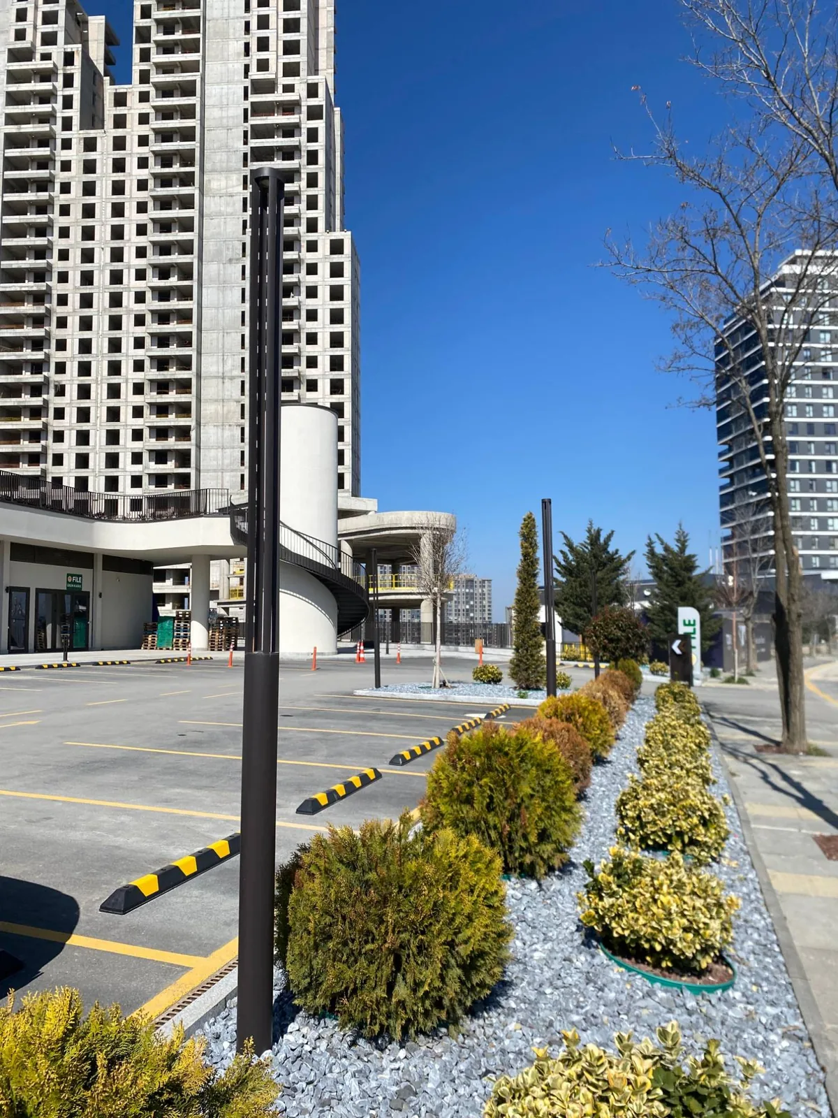 Tona Residence — Slim bollard-poles line the retail forecourt and parking, carrying the warm light down to the street.