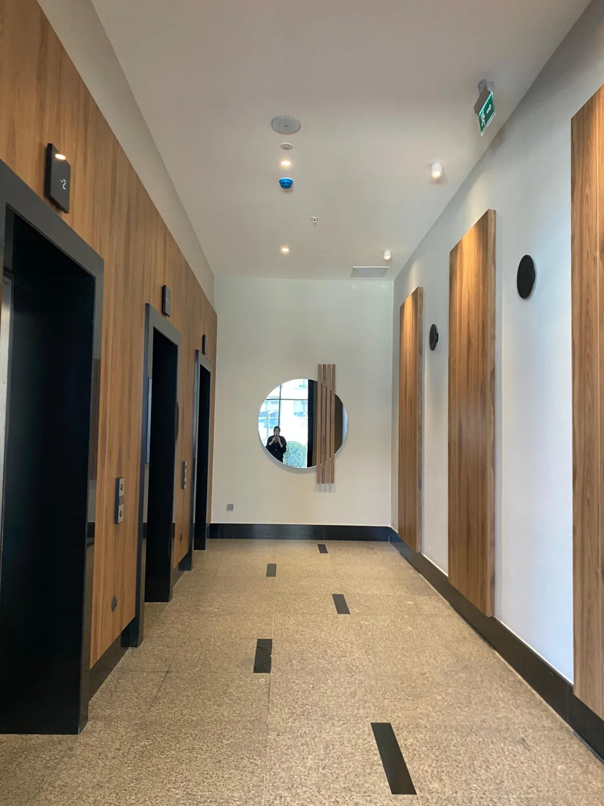 Tona Residence — A lift lobby reads calm and hotel-like — downlights, black surface spots and a wall light on walnut.