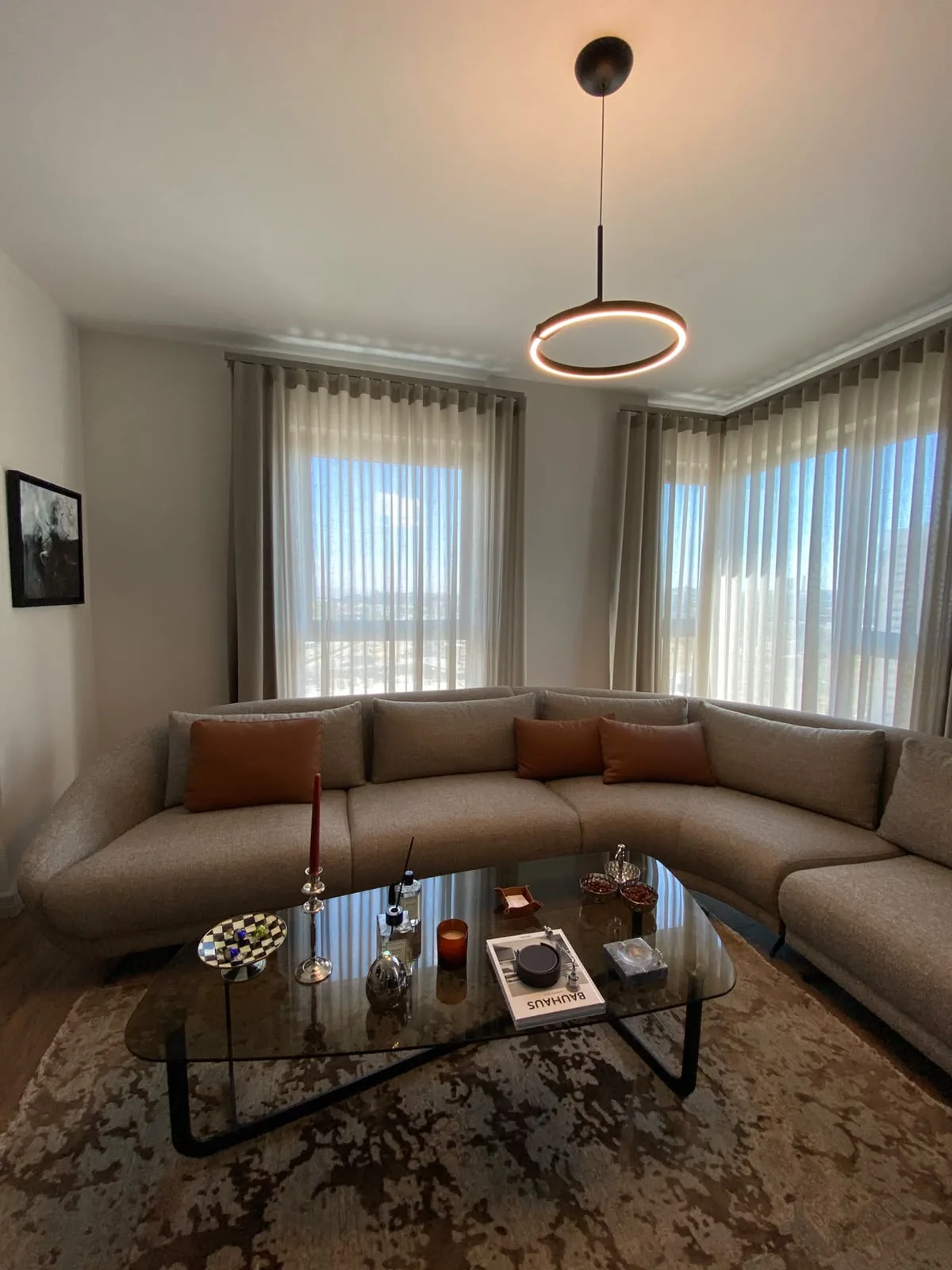 Tona Residence — A ring pendant floats over the living room, a single warm circle against the corner glazing.